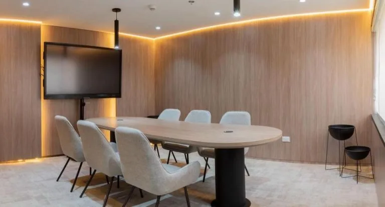 Sala de juntas con franja de luz cálida sobre el panel de madera, a ras de techo y de piso, en la Torre Tequendama