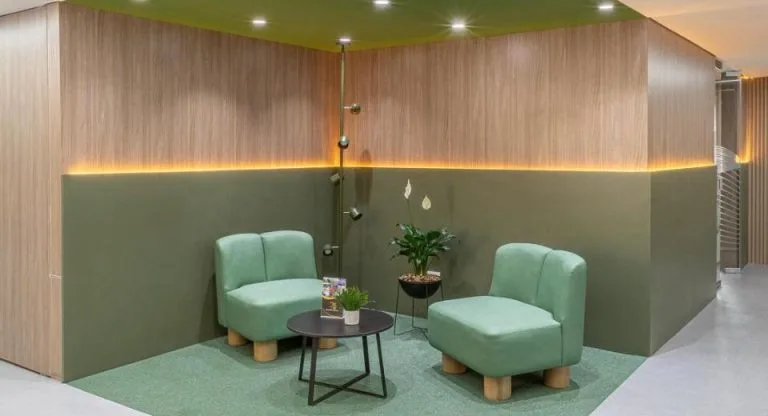Zona de espera con sillones verdes y franja de luz cálida bajo paneles de madera, oficinas Torre Tequendama