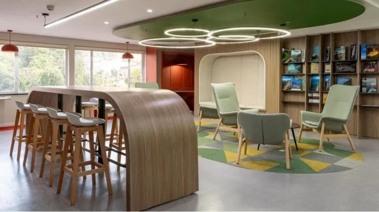 Cafetería y zona de lectura en la Torre Tequendama con aros LED suspendidos sobre círculo verde y barra de madera