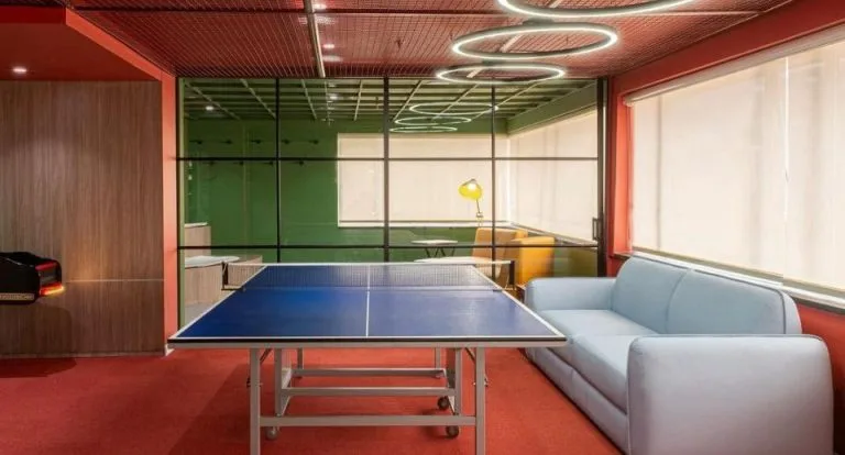 Salón con mesa de ping-pong en la Torre Tequendama, con aros LED suspendidos en el techo rojo y sofá gris
