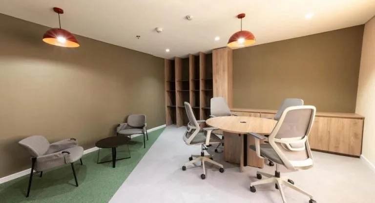 Sala de reuniones informal en la Torre Tequendama con dos lámparas colgantes cobrizas, mesa redonda y estantería