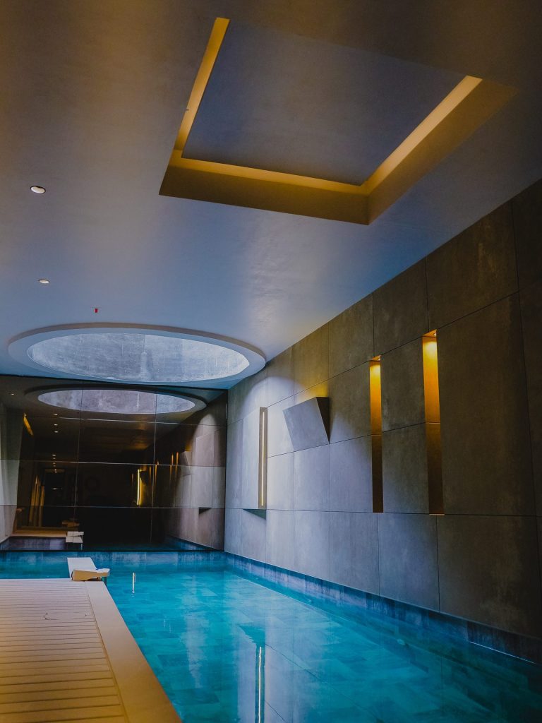 Zona de piscina con luz indirecta en techo y ventana circular, Edificio Tempo, iluminación Asombra