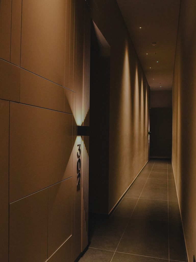 Pasillo con luminarias de pared y luz cálida, Edificio Tempo, iluminación Asombra