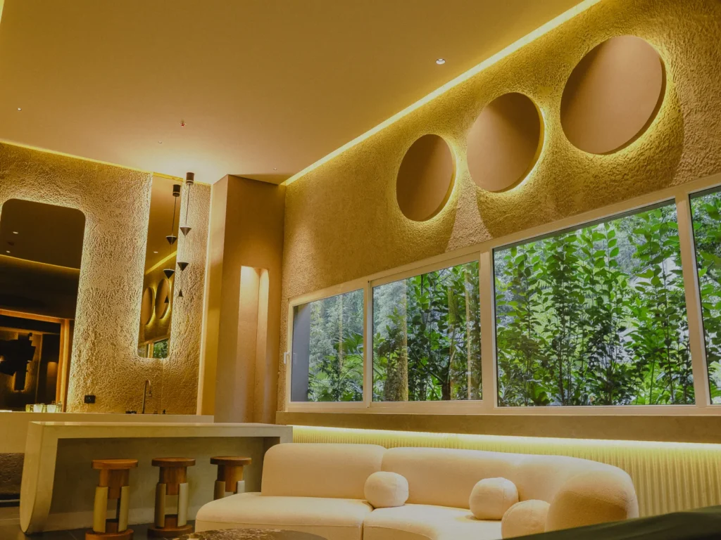 Sala con muros texturizados, nichos circulares y luz LED indirecta cálida, proyecto iluminado por Asombra